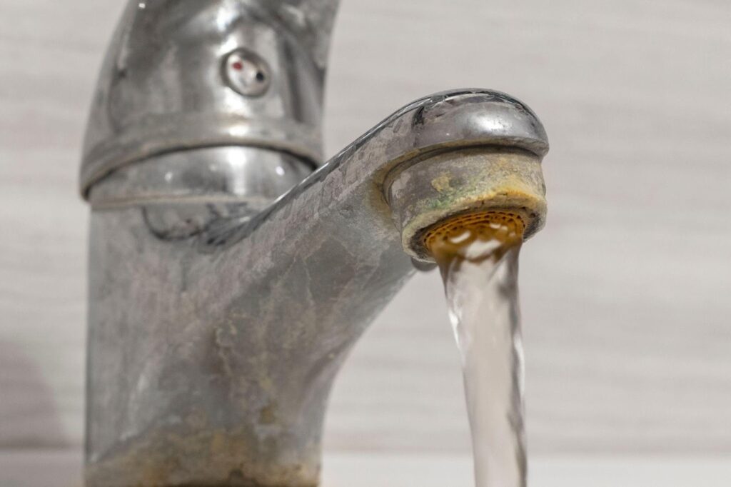 Close-up of a faucet with water flowing highlighting the stream and the shiny metal surface