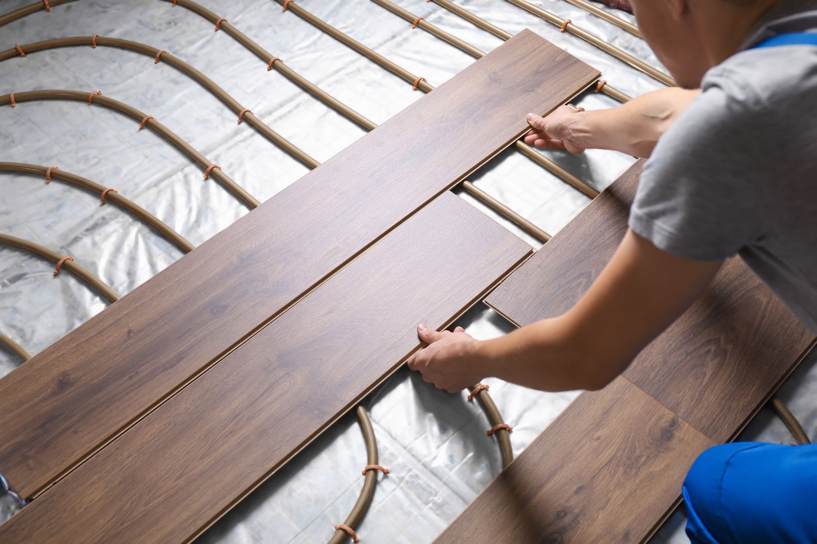A man installing wood flooring over radiant floor heating systems in a home setting.