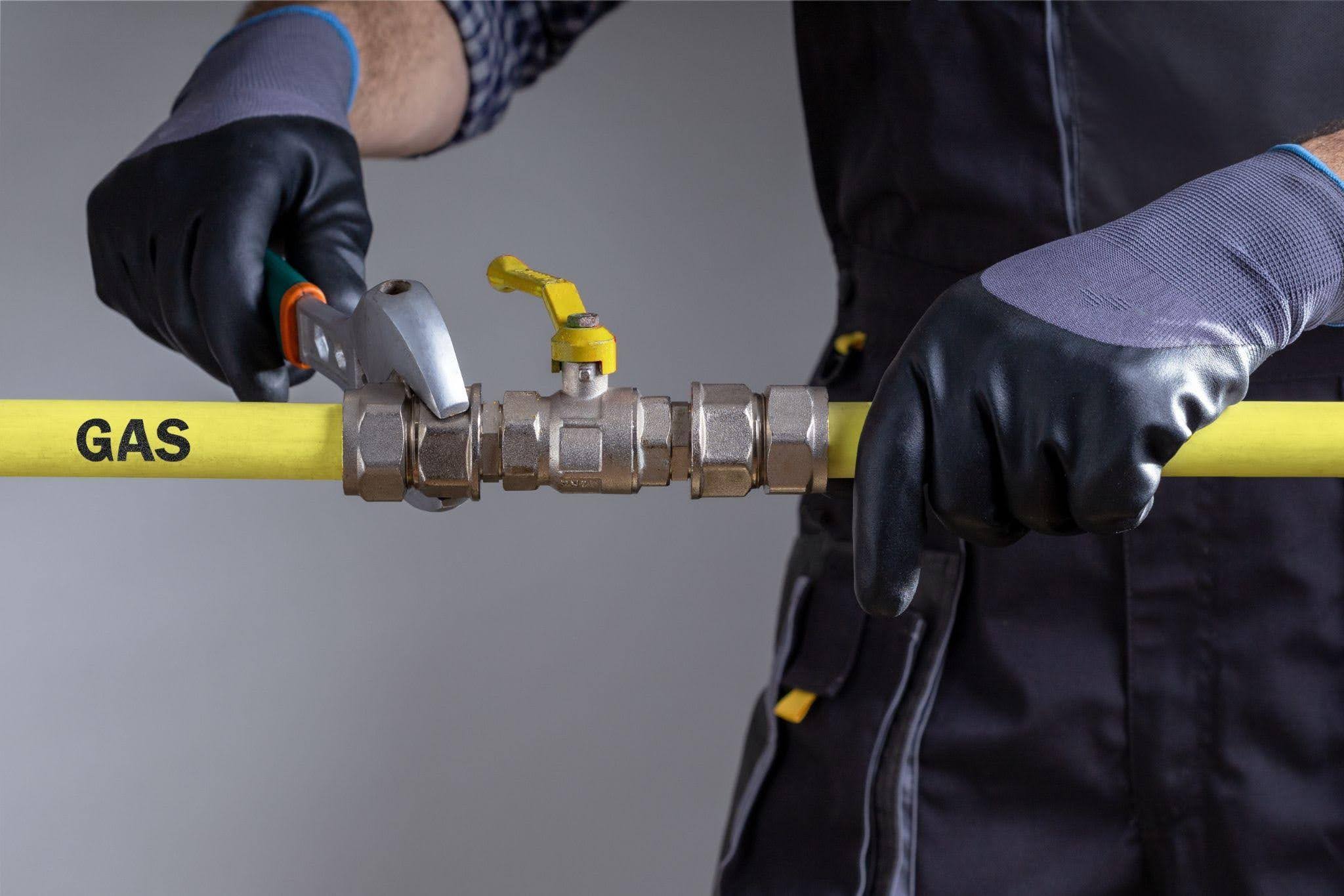 A man in black overalls and gloves holds a yellow pipe standing in a work environment