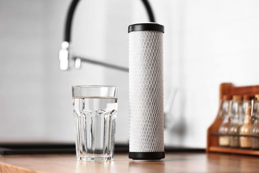 A countertop displays a water filter adjacent to a glass of water highlighting water purification for safe drinking