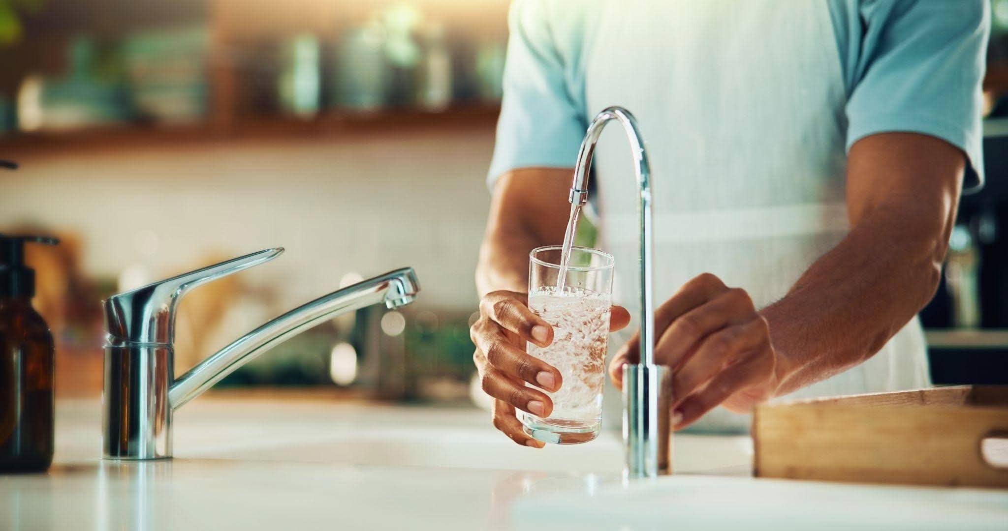 A hand grasping a glass filled with water emphasizing the act of drinking