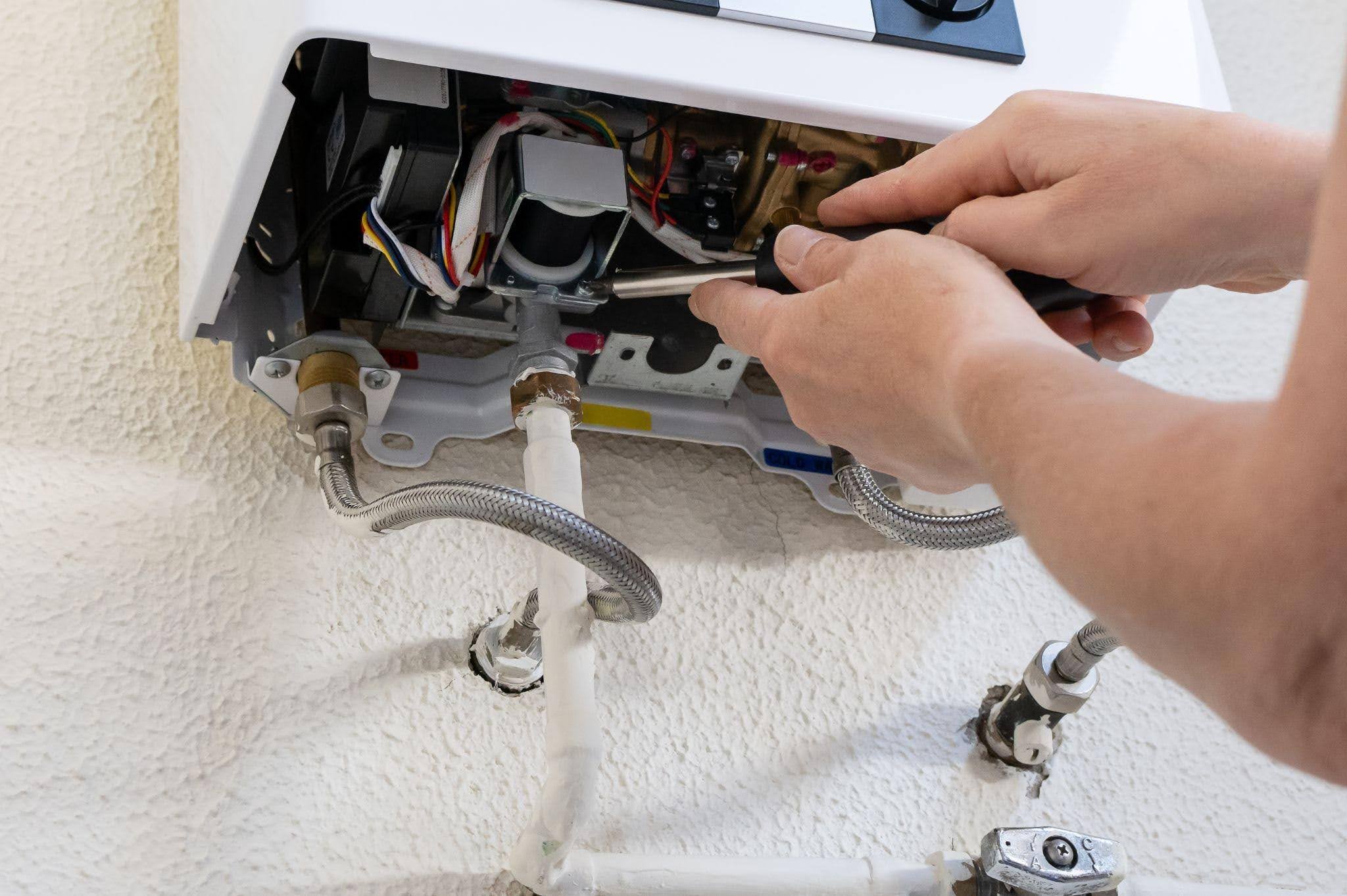 A technician repairs a water heater using tools and inspecting the unit for issues in a residential setting