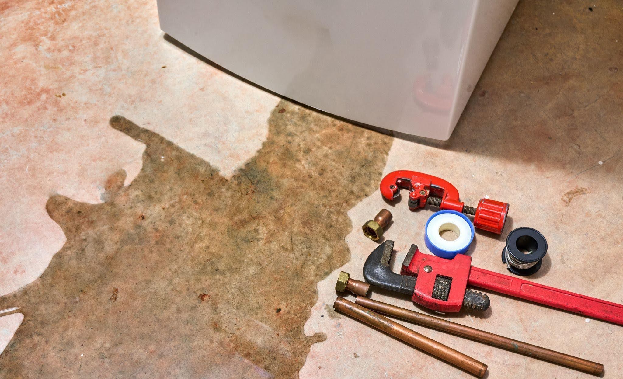 A water heater with wrenches and pliers arranged on the floor indicating a maintenance or repair setting