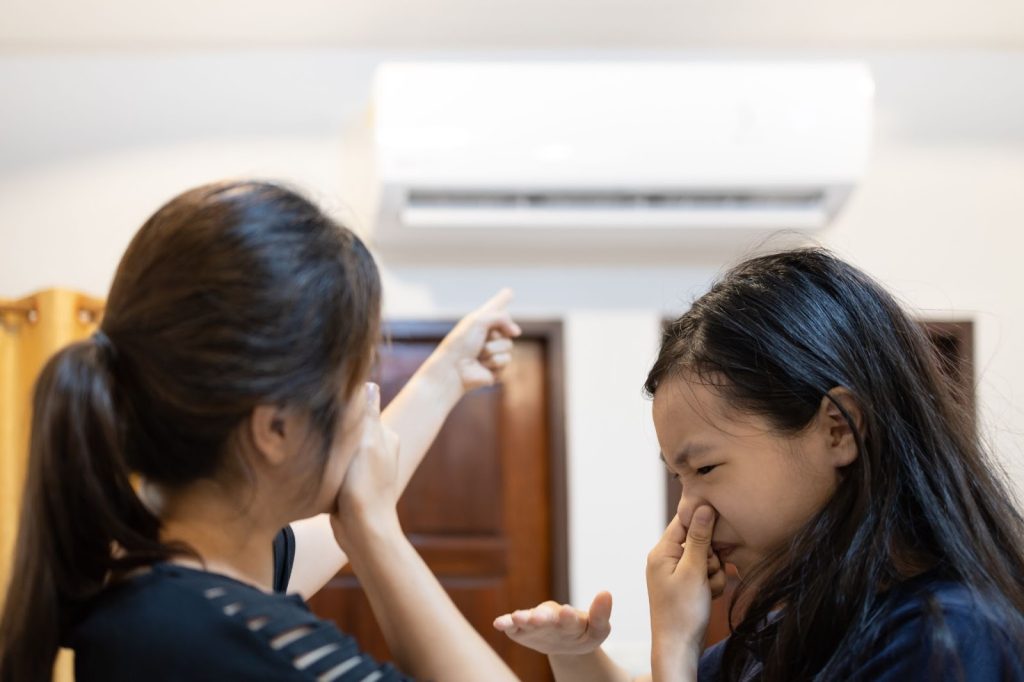 Two women feeling cool air from air conditioner, checking for gas leaks near gas line