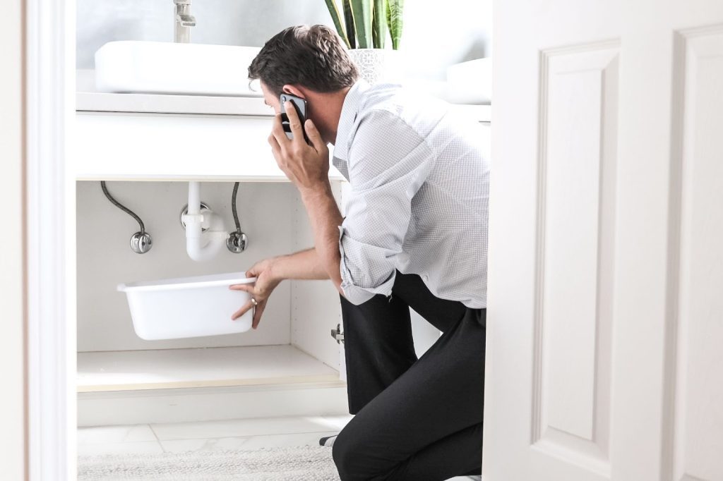 A man in a bathroom with a sink, making a call about plumbing services for apartment development
