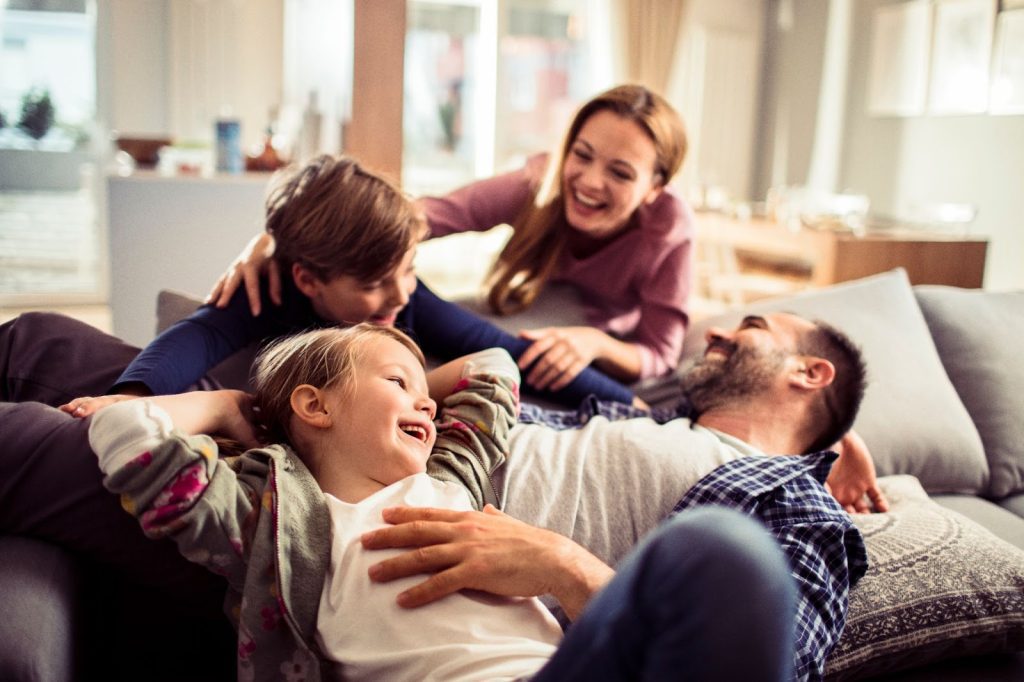 Family bonding on a cozy couch, feeling the benefits of radiant floor heating in their home