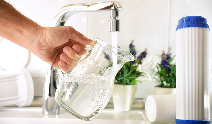 A person holding a pitcher of water from a faucet, emphasizing water treatment systems and residential water quality