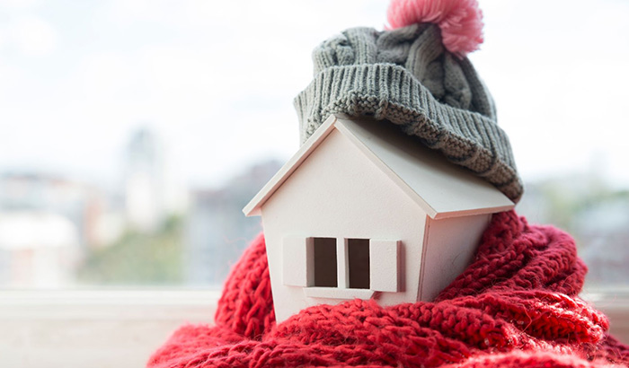 A small house with a hat and scarf on top, symbolizing radiant heating and traditional forced air heating systems