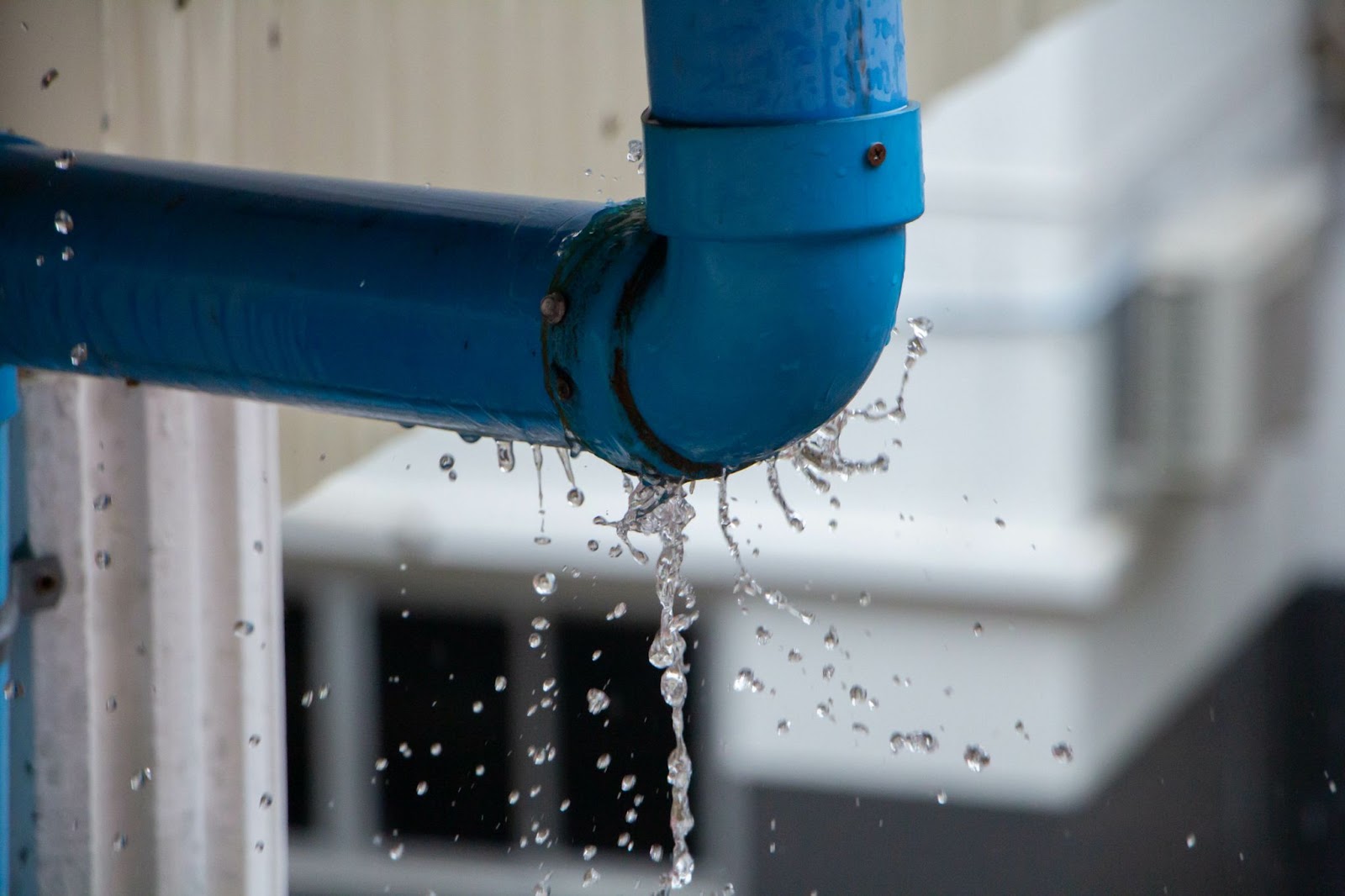 Water leaking from a blue pipe joint outside a building.