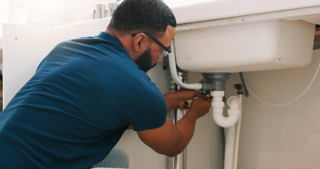 A man is working on a bathroom sink using tools to address plumbing problems