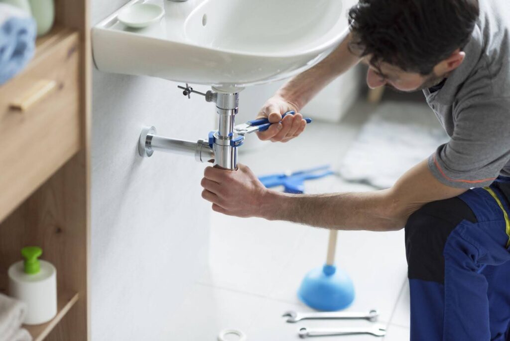 A man repairs a sink in a bathroom focused on fixing plumbing issues with tools in hand