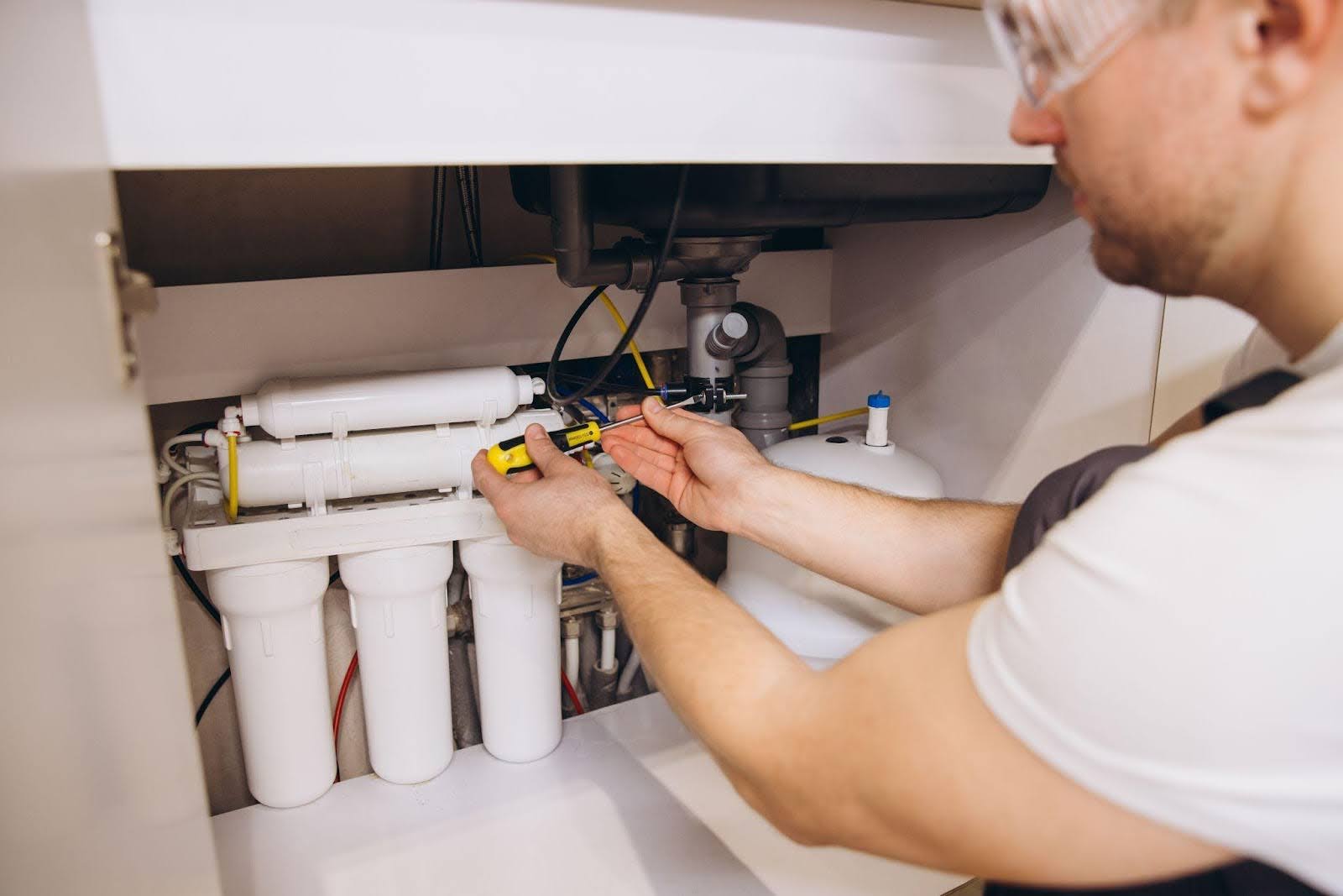 A man repairs a water filter in a modern kitchen surrounded by utensils and appliances