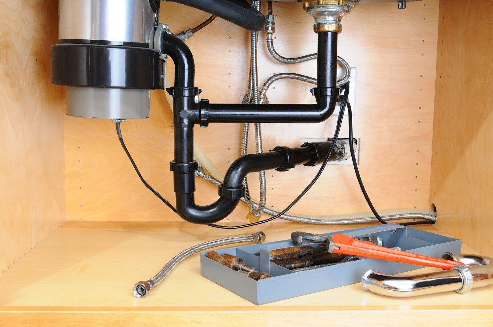 A sink beneath a cabinet accompanied by a toolbox and visible plumbing pipes