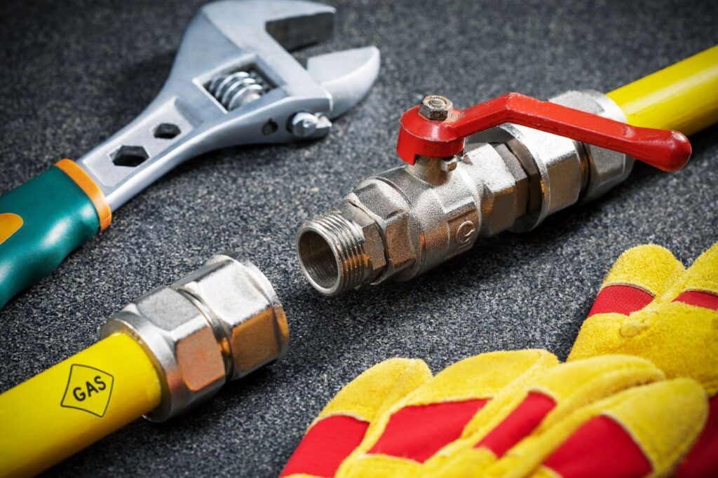 Gloves, a wrench, and a pipe on a workbench indicating a plumbing task