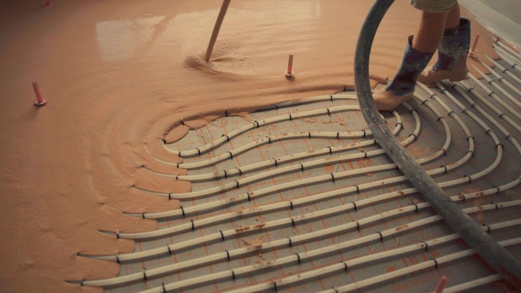 A person uses a hose to apply material while laying a floor in a construction setting
