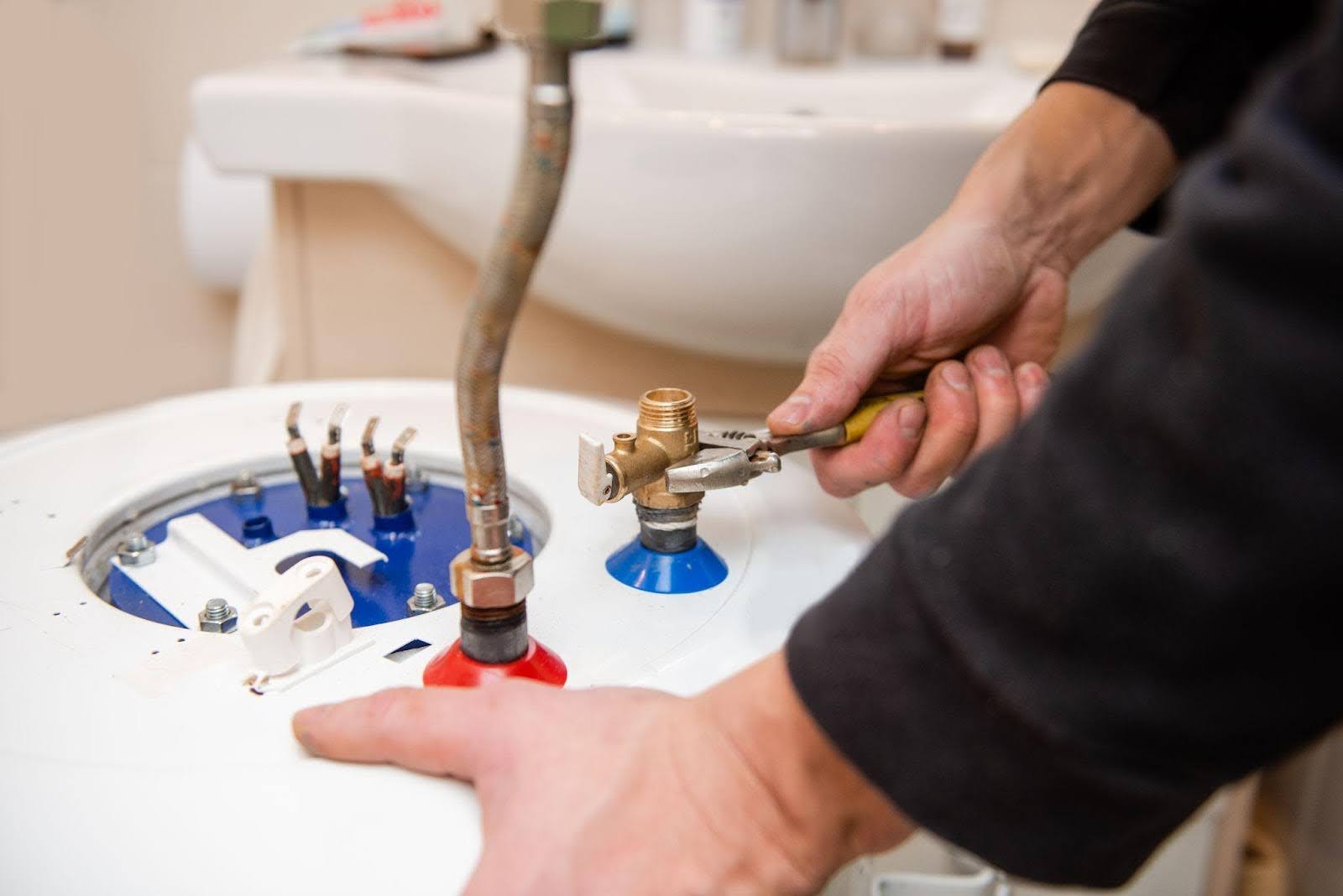 A man is engaged in fixing a water heater in a bathroom with various tools nearby