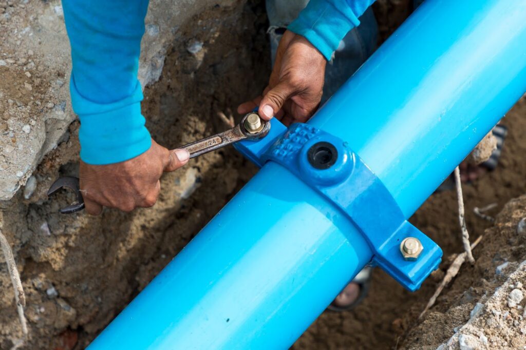 Worker tightening a blue pipeline joint with a wrench in a trench.
