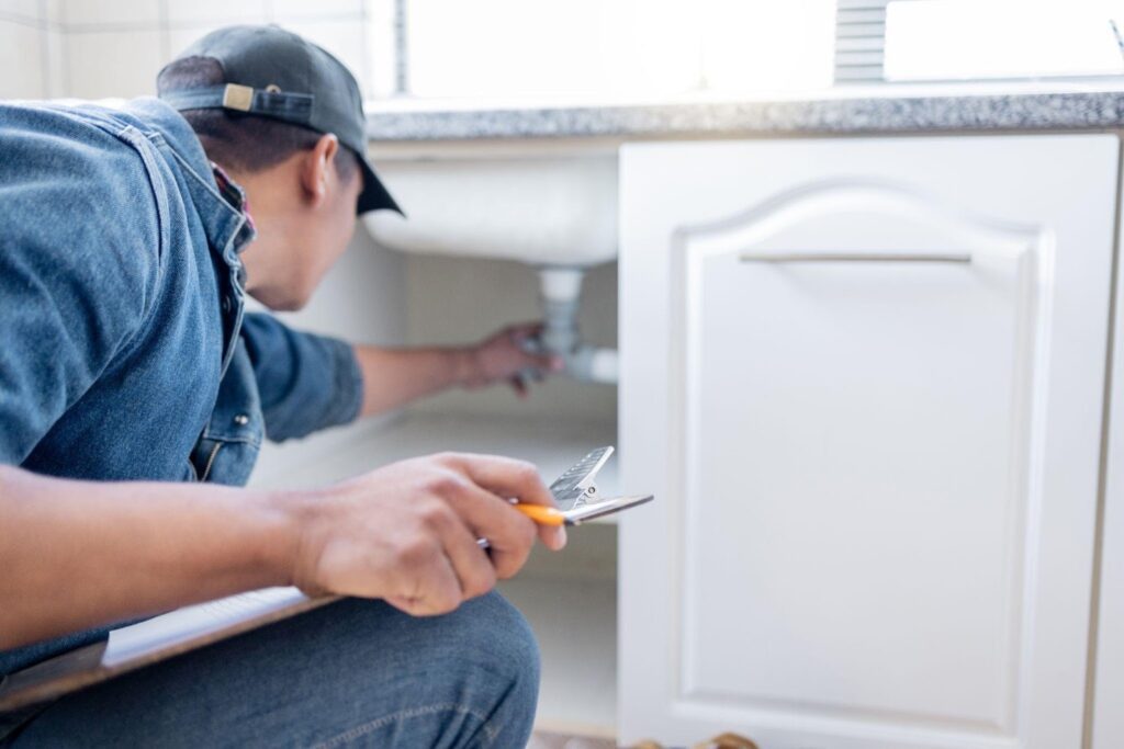 A man in a blue shirt and cap is engaged in fixing a sink demonstrating his plumbing skills