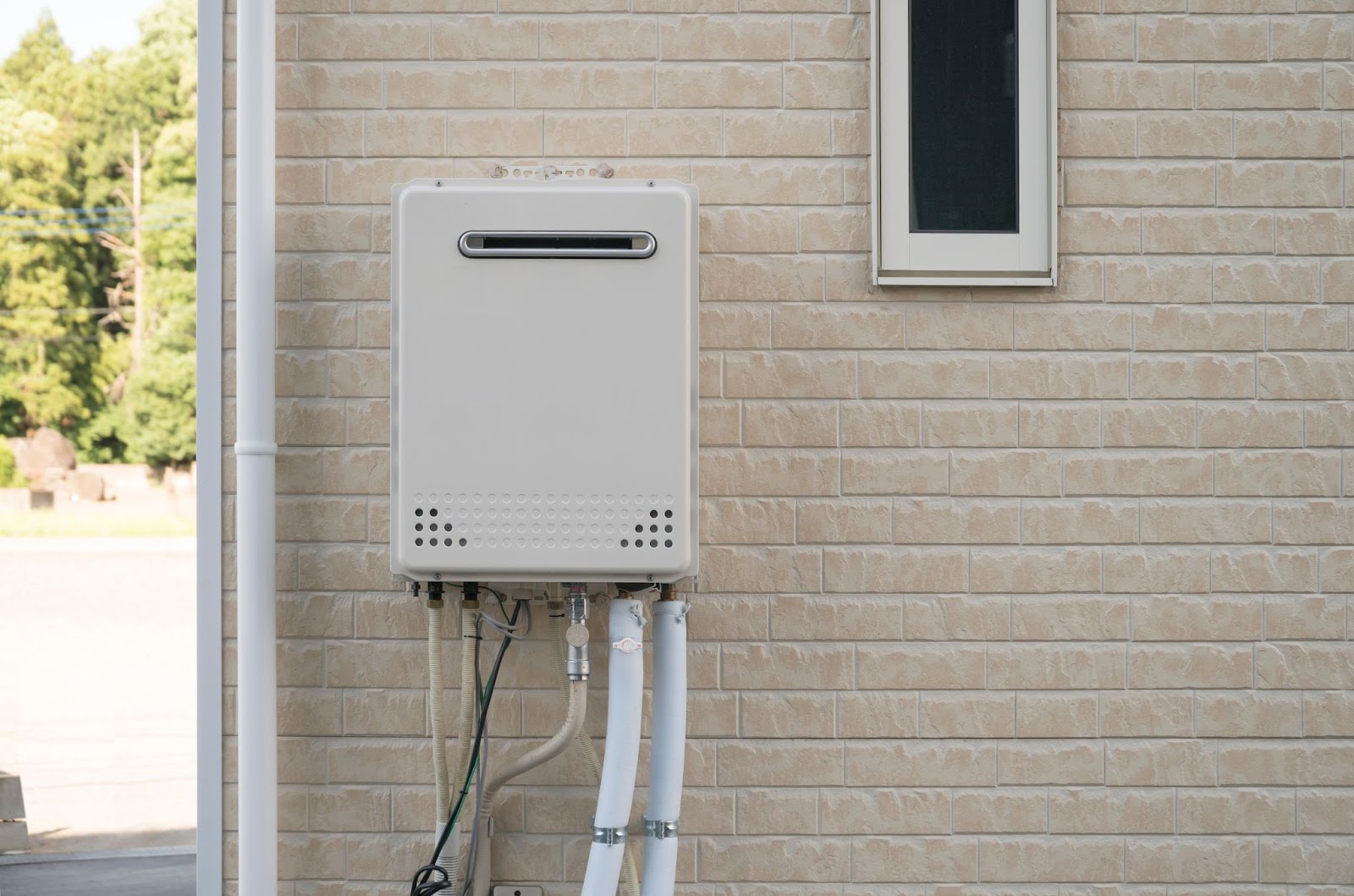 A gas water heater installed on the exterior wall of a house, showcasing its functional design and outdoor placement.