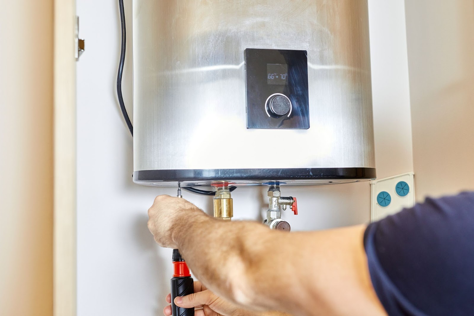 A man works on fixing a water heater, using tools and inspecting the unit for repairs.