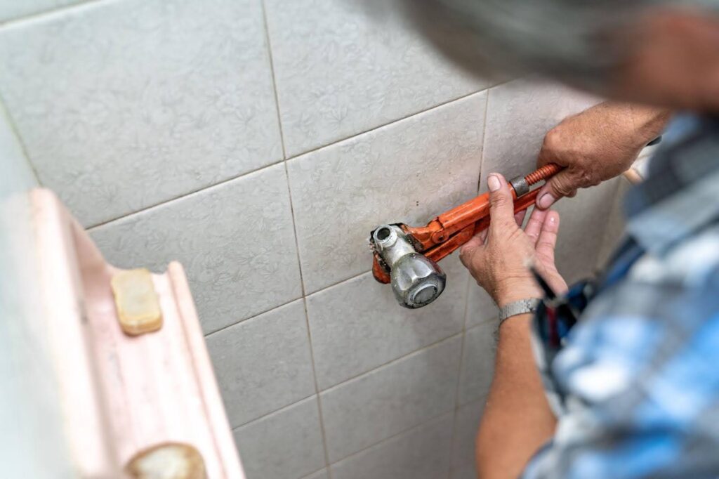 A man repairs a toilet with a wrench, concentrating on the task at hand