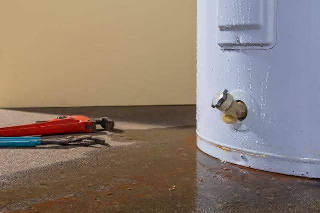 A white water heater with noticeable rust and a small puddle on the floor