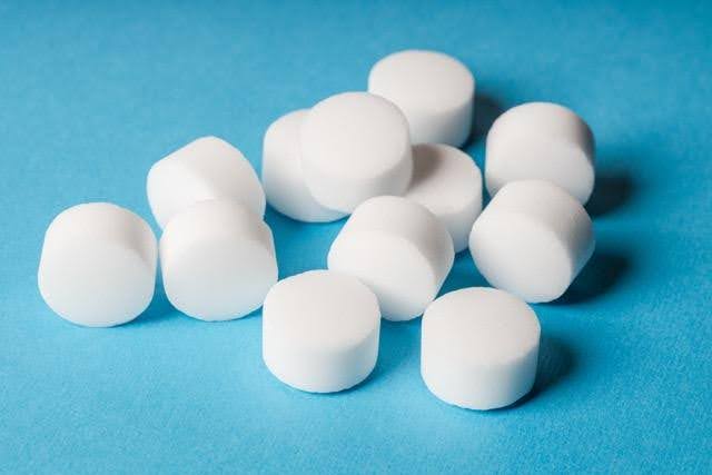 Twelve white cylindrical tablets on a bright blue background evenly scattered
