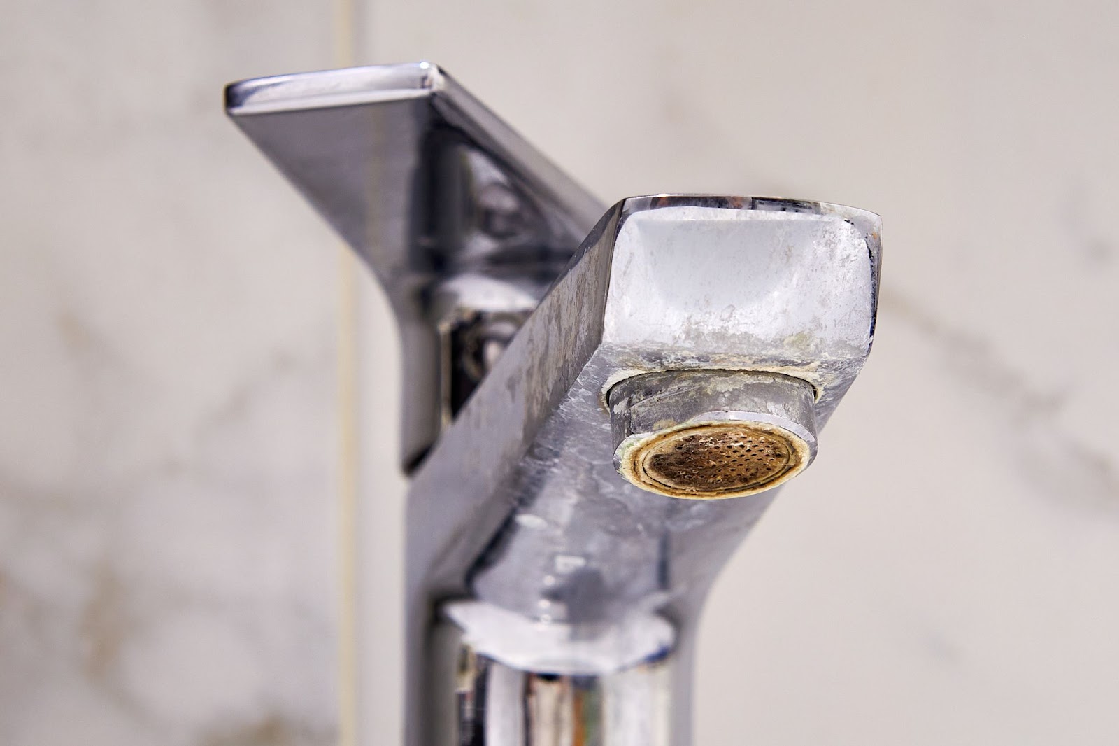 A close-up view of a chrome bathroom faucet heavily covered in white limescale and mineral buildup.