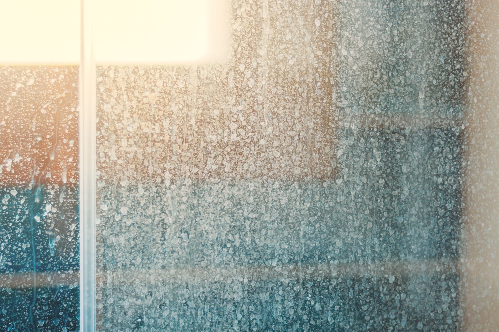 A close-up view of a glass shower door covered in dried white water spots and mineral deposits.