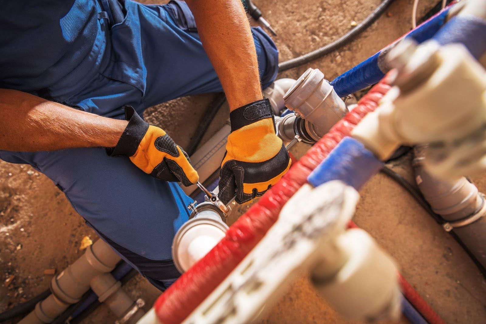 A man in blue overalls is repairing a pipe focused on his work with tools in hand