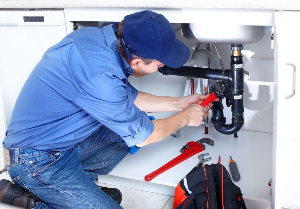 A man is engaged in repairing a sink positioned beneath it with various tools