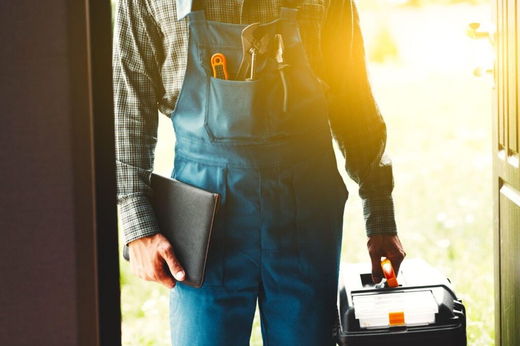 A man wearing overalls holds a toolbox and a clipboard prepared for work or a project