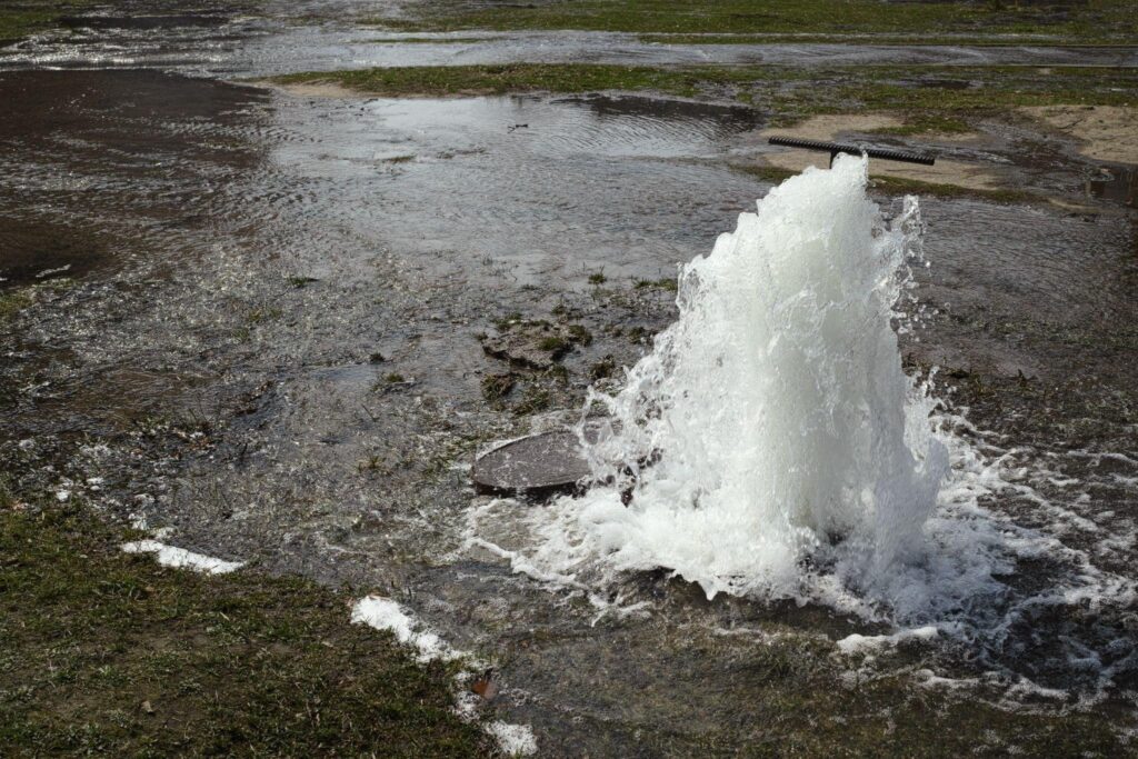 Water shoots high into the air from an open fire hydrant on a city street