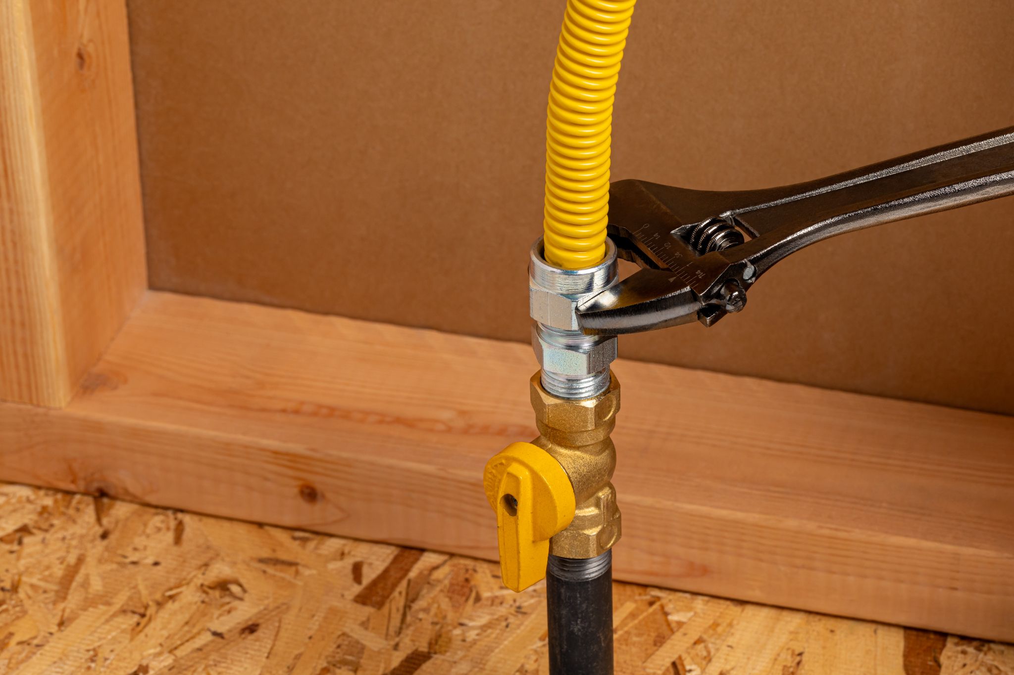An adjustable wrench tightening a metal fitting connecting a flexible yellow gas line to a brass shut-off valve.