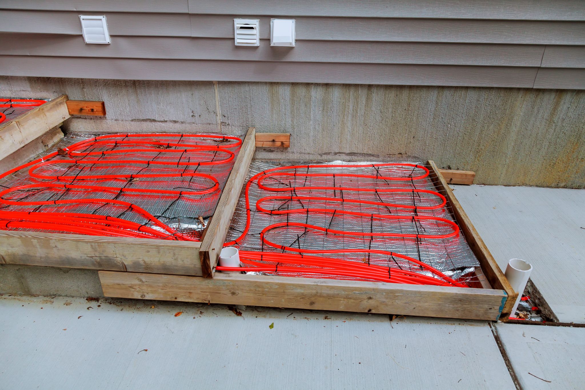 Installation of red radiant PEX heating tubing laid over insulation panels for outdoor snow melting steps.