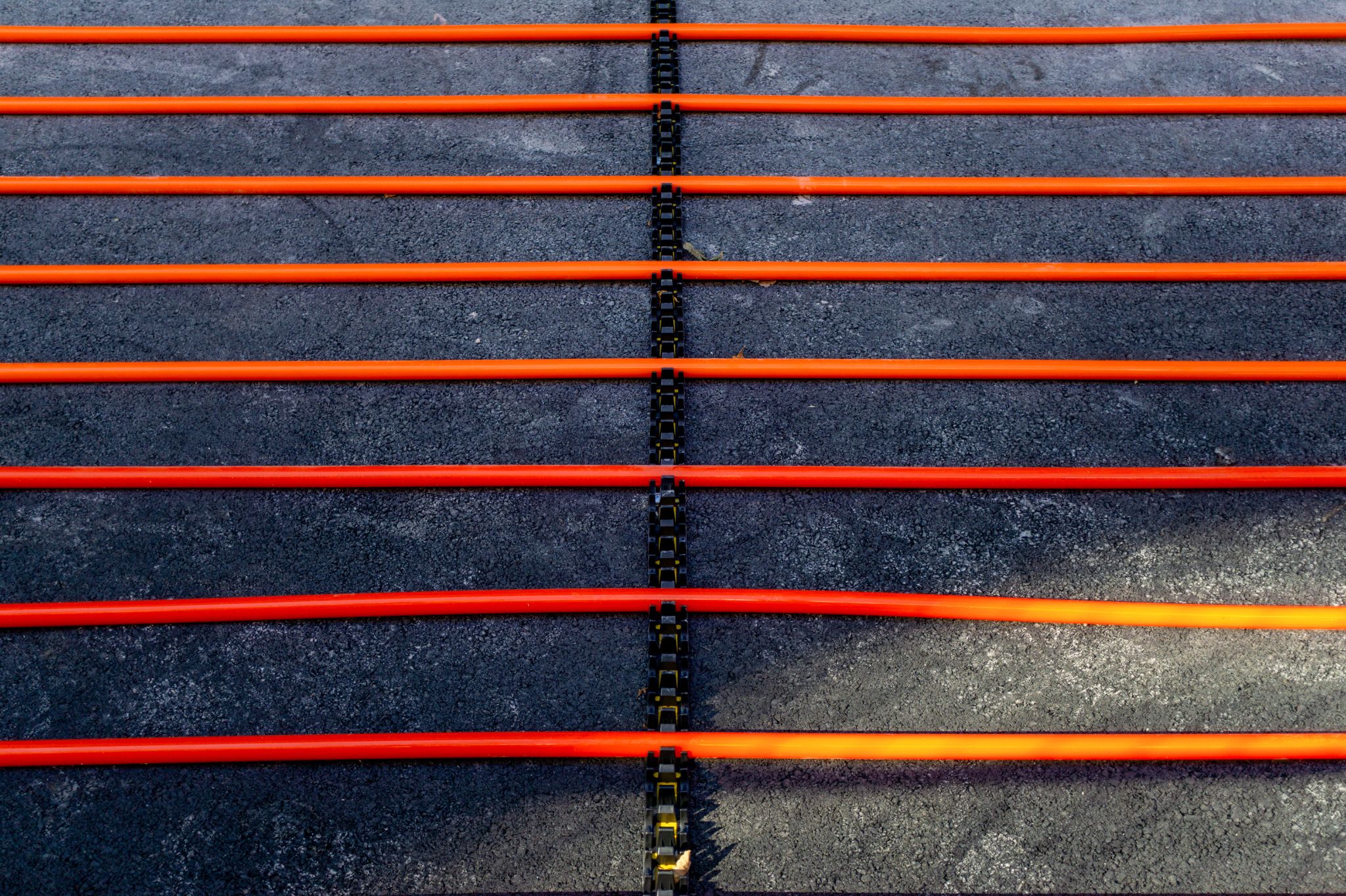 Parallel orange heating cables secured in black track strips on asphalt for a snow melting system.